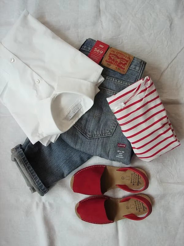 Flatlay of a white shirt, jeans, striped top, and red sandals for an occasion outfit