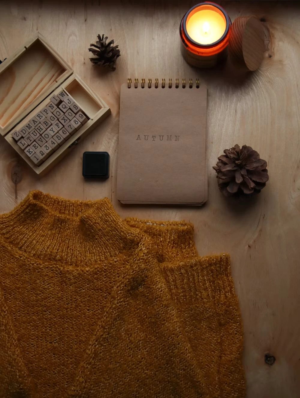Autumn-themed flatlay with a mustard knit sweater, candle, and seasonal notebook