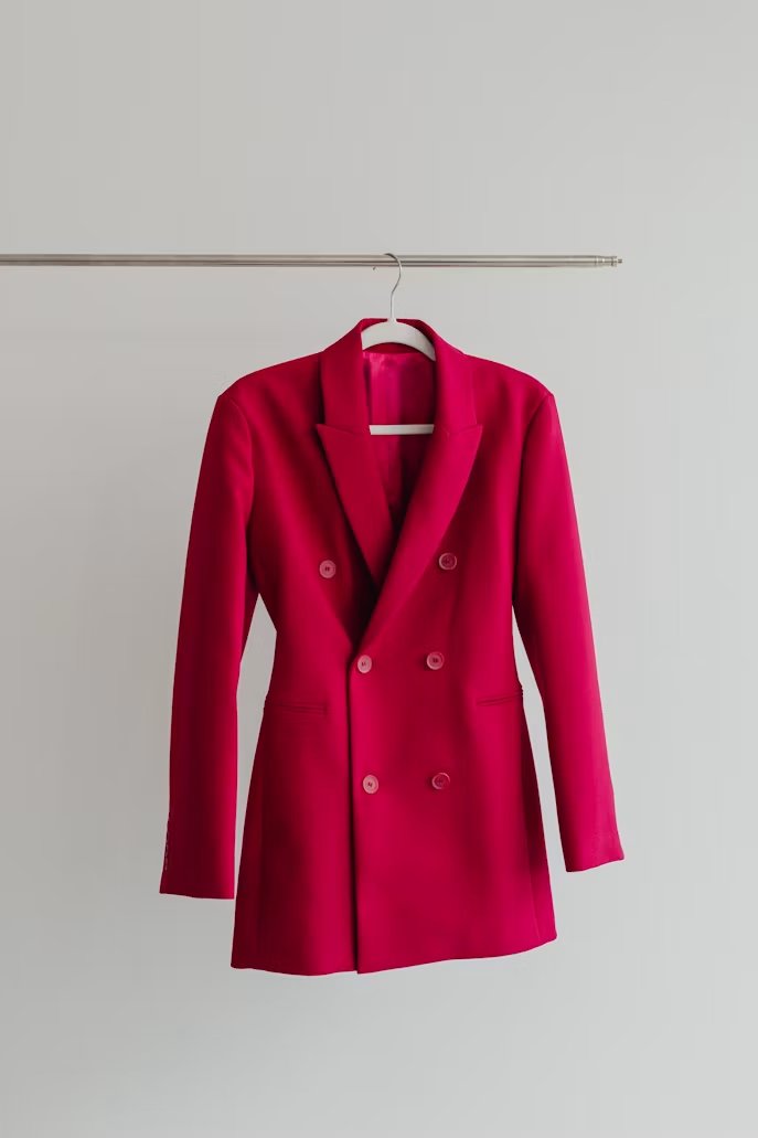 A single red blazer dress hanging against a plain wall