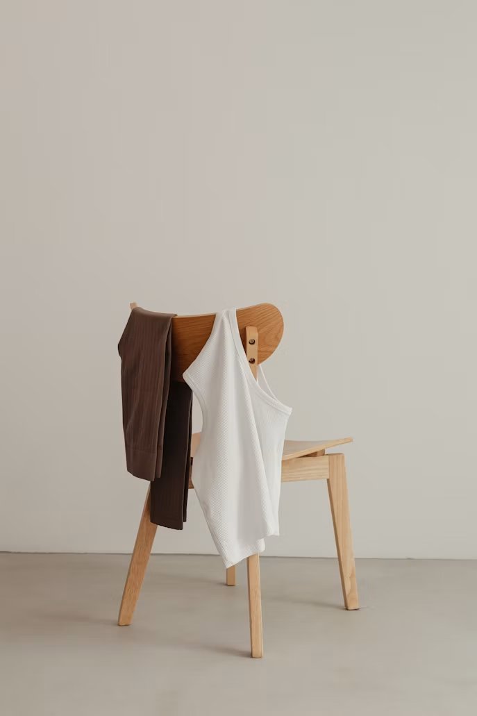 Wooden chair with a brown pant and white tank top draped over it, minimal styling