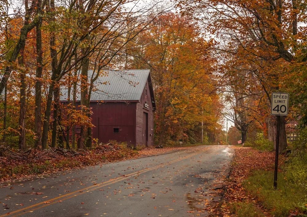 New England country road lined with autumn foliage near a red barn